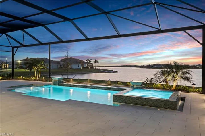 Pool at dusk with pool water feature, a patio, glass enclosure, and a water view