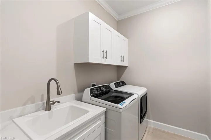 Laundry area featuring cabinets, ornamental molding, separate washer and dryer, and sink