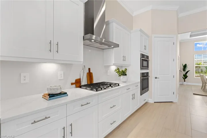 Kitchen featuring appliances with stainless steel finishes, white cabinets, light stone counters, crown molding, and wall chimney range hood