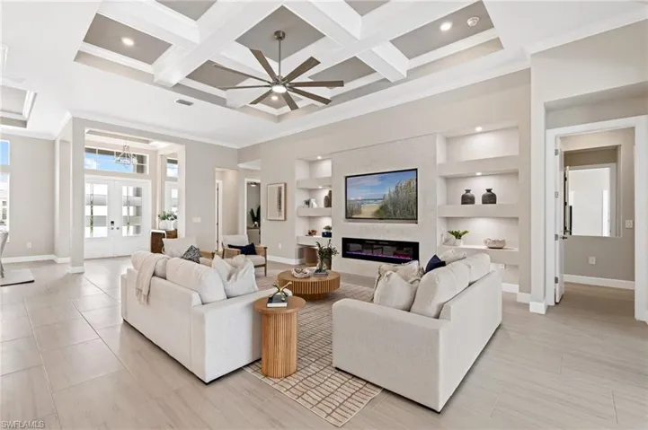 Tiled living room with french doors, a large fireplace, coffered ceiling, crown molding, and built in shelves