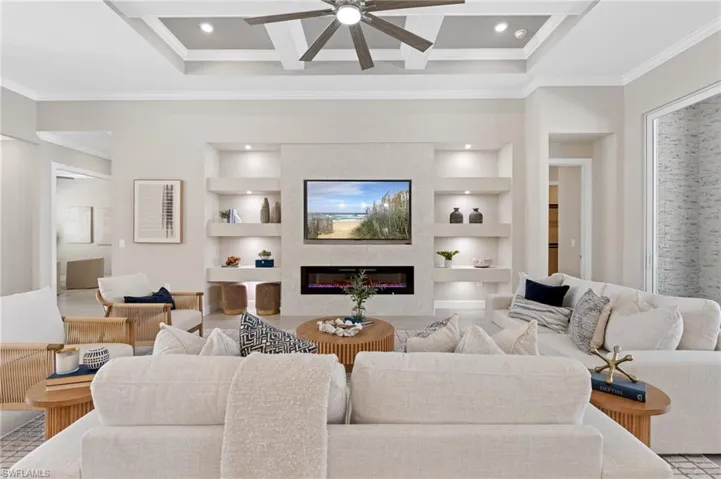 Living room with crown molding, coffered ceiling, a fireplace, and built in shelves