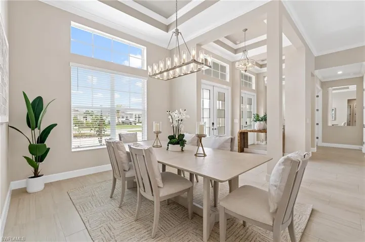 Dining space with french doors, ornamental molding, a raised ceiling, a notable chandelier, and a towering ceiling