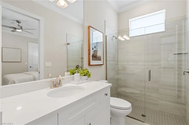 Bathroom featuring crown molding, ceiling fan, vanity, a shower with shower door, and toilet