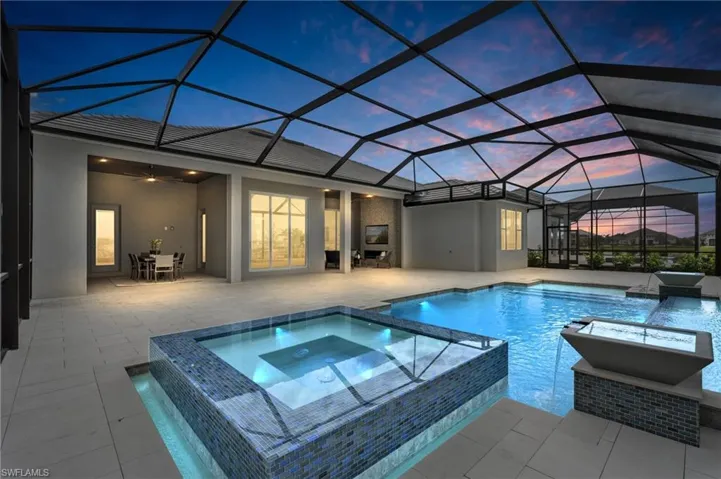 Pool at dusk with an in ground hot tub, ceiling fan, glass enclosure, and a patio
