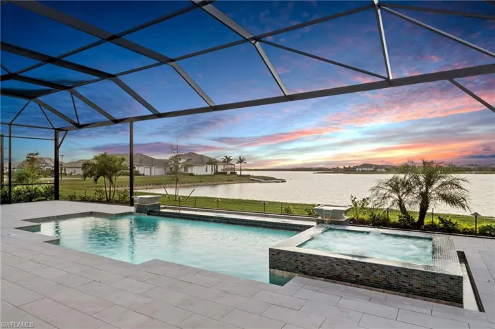 Pool at dusk featuring a patio area, pool water feature, glass enclosure, and a water view