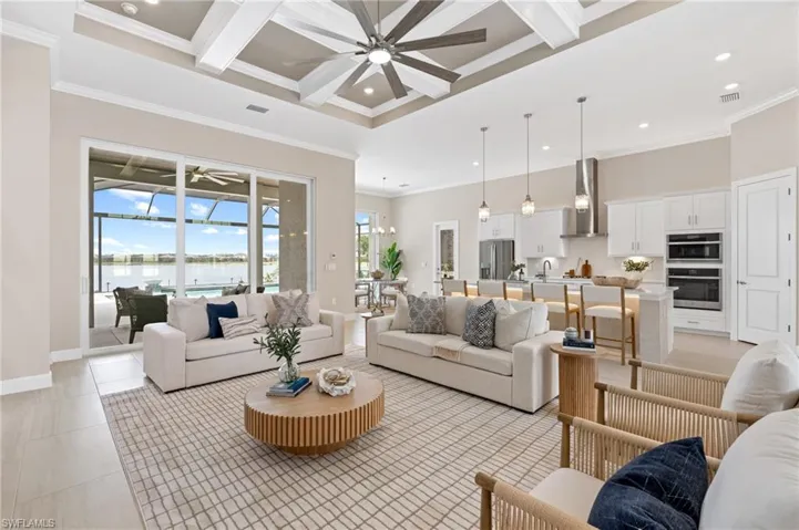 Tiled living room with coffered ceiling, a water view, ceiling fan, ornamental molding, and a towering ceiling