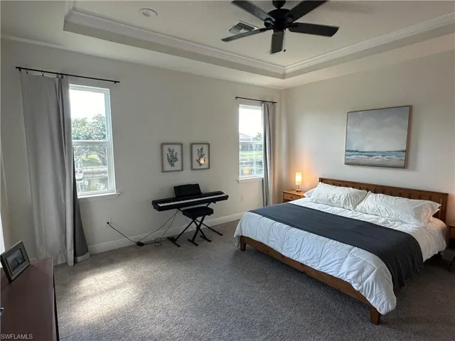 Carpeted bedroom featuring a tray ceiling, multiple windows, crown molding, and ceiling fan