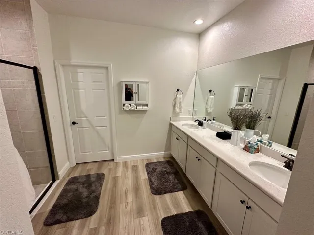 Bathroom featuring a shower stall, light wood finished floors, double vanity, and a textured wall
