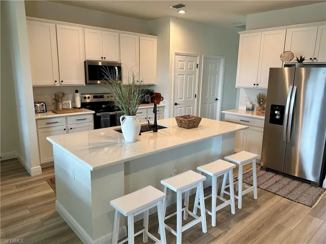 Kitchen with a breakfast bar, stainless steel appliances, white cabinets, light wood-style flooring, and light stone countertops