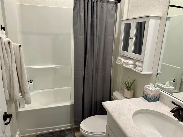 Bathroom featuring shower / bath combo with shower curtain, vanity, a textured wall, and dark wood finished floors