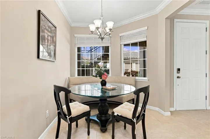 Bay window breakfast nook featuring neutral tile flooring, crown molding, multi-paned windows, and a central chandelier