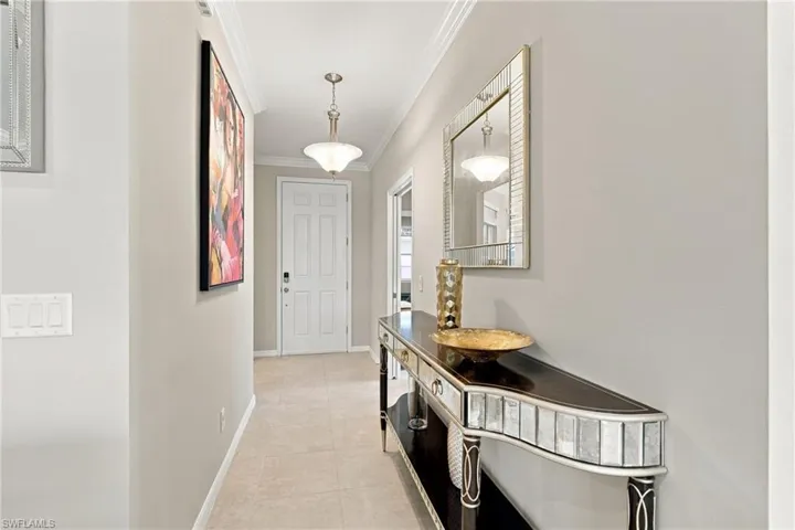 Entryway featuring neutral-toned tile flooring, crown molding, a semi-flush mount light fixture, and a solid-core six-panel door