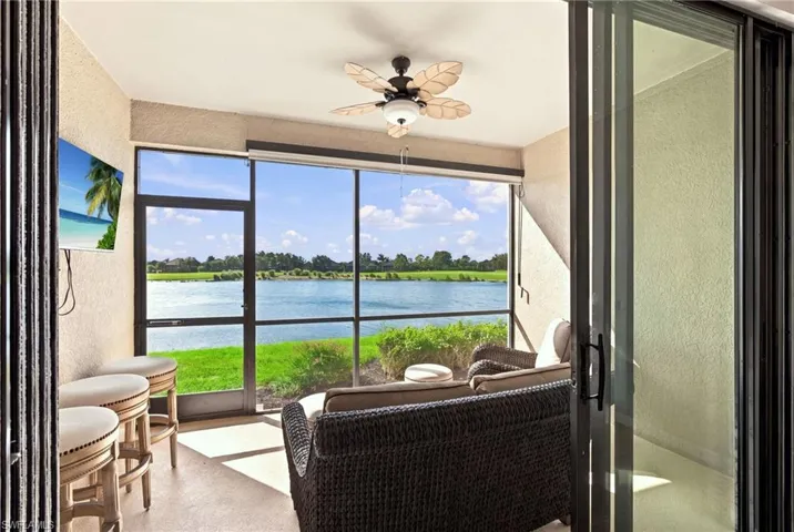 Enclosed patio featuring floor-to-ceiling screened panels, built-in wall mount for electronics, and a ceiling fan with leaf-shaped blades, overlooking a water feature and landscaped lawn