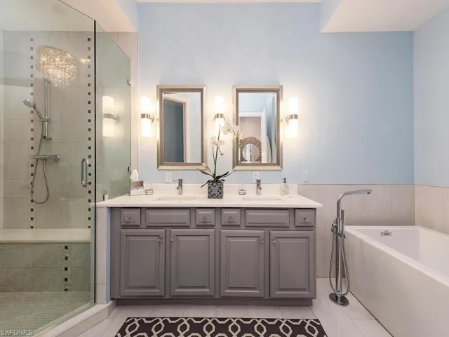 Bathroom featuring a soaking tub, a stall shower, double vanity, light tile patterned flooring, and wainscoting