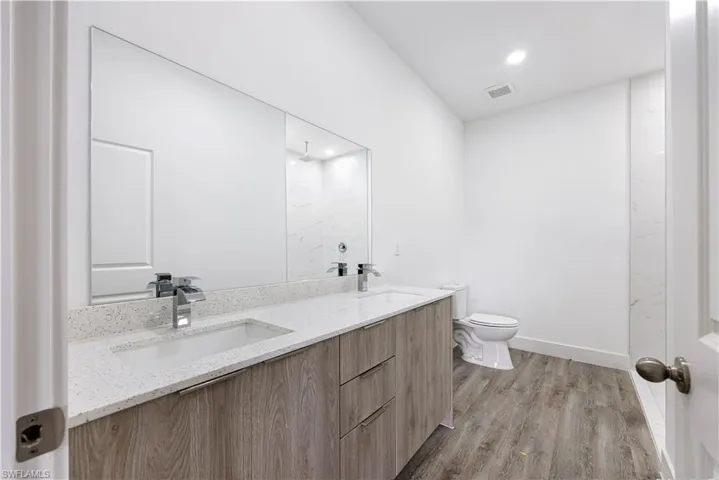 Bathroom featuring walk in shower, dark wood-style flooring, double vanity, and recessed lighting