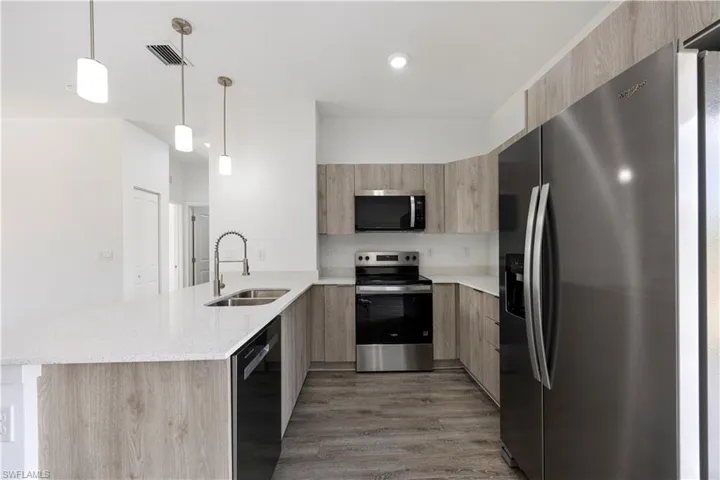 Kitchen with stainless steel appliances, modern cabinets, light stone counters, hanging light fixtures, and light wood-style floors