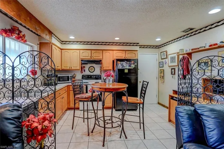 Kitchen featuring light brown cabinets, under cabinet range hood, range with electric stovetop, light countertops, and freestanding refrigerator
