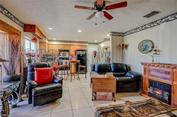 Living room with light tile patterned floors, visible vents, a ceiling fan, a glass covered fireplace, and a textured ceiling