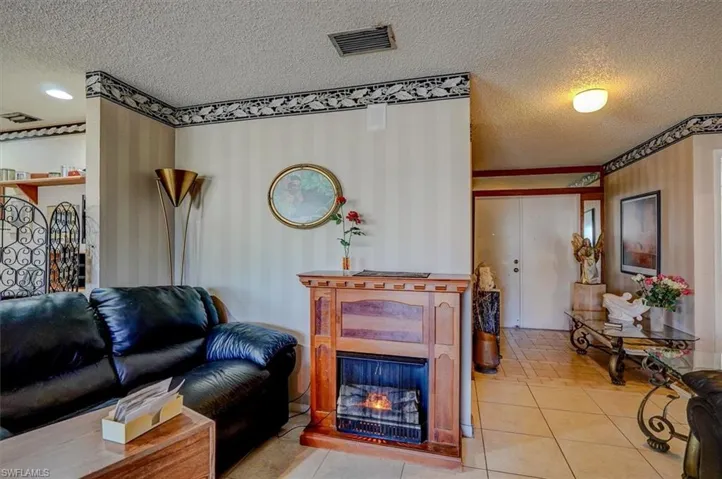 Living area featuring a textured ceiling, a warm lit fireplace, light tile patterned flooring, and visible vents