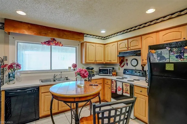 Kitchen with under cabinet range hood, light countertops, light brown cabinetry, black appliances, and a sink