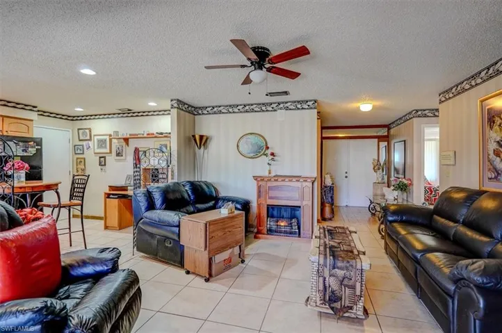 Living area featuring a ceiling fan, a glass covered fireplace, light tile patterned flooring, and a textured ceiling