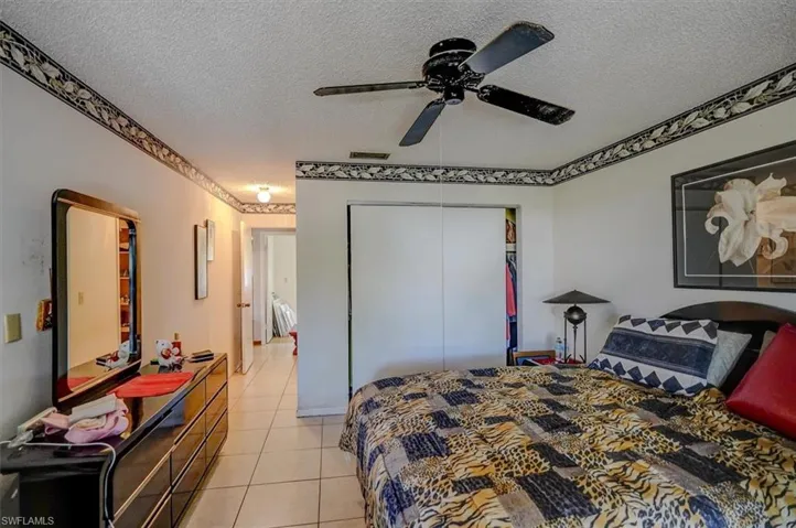 Bedroom with a textured ceiling, light tile patterned flooring, visible vents, a ceiling fan, and a closet