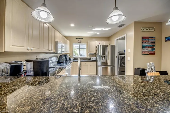 Kitchen featuring stone countertops, stainless steel refrigerator, light-toned cabinetry, and dual pendant lighting fixtures