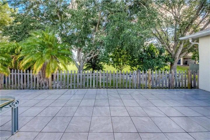 Tiled patio featuring a wood-style picket fence, mature trees, and palm landscaping