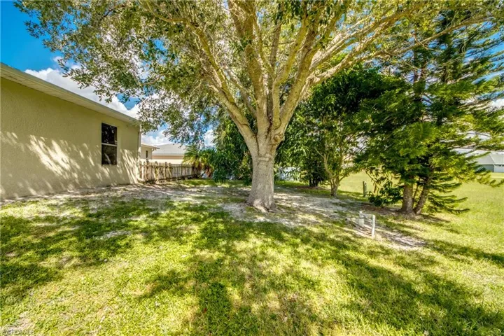 Exterior side yard featuring mature shade trees, a grass lawn, and wood-panel fencing