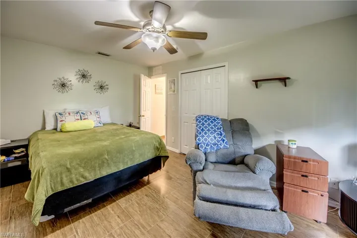 Wood-finish tile flooring, ceiling fan with integrated light fixture, dual-panel closet doors, and wall-mounted shelving