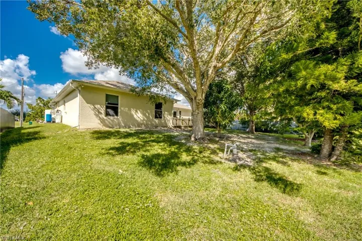 Stucco exterior residence featuring a hipped roofline, expansive lawn, and mature shade trees