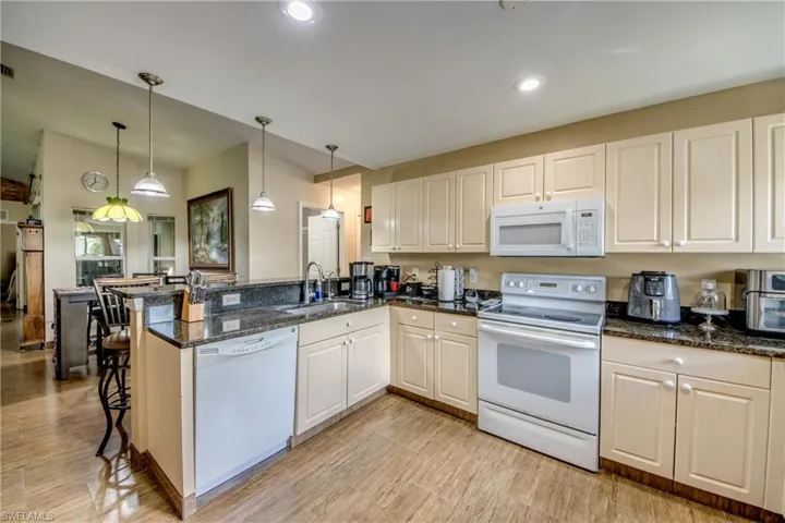 Kitchen featuring raised-panel cabinetry, dark stone-finish countertops, tile flooring, and integrated pendant lighting