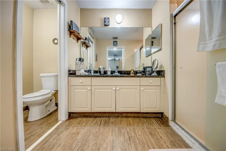 Bathroom featuring wood-finish flooring, vanity with stone-surfaced countertop, integrated sink, and an enclosed shower with glass door