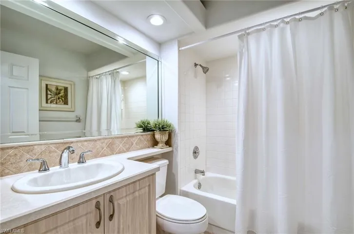 Bathroom with vanity, shower / tub combo, and decorative backsplash