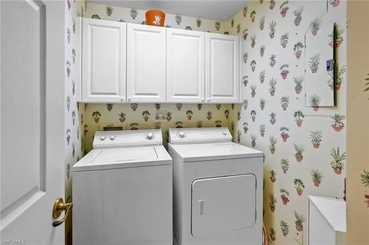 Washroom featuring wallpapered walls, cabinet space, and washer and clothes dryer