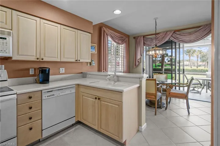 Kitchen featuring white appliances, a peninsula, light countertops, light tile patterned floors, and hanging light fixtures