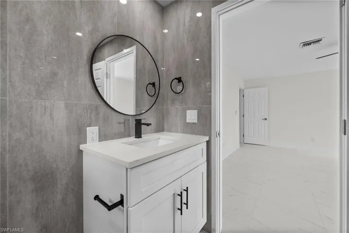Bathroom featuring vanity, light marble finish flooring, and tile walls