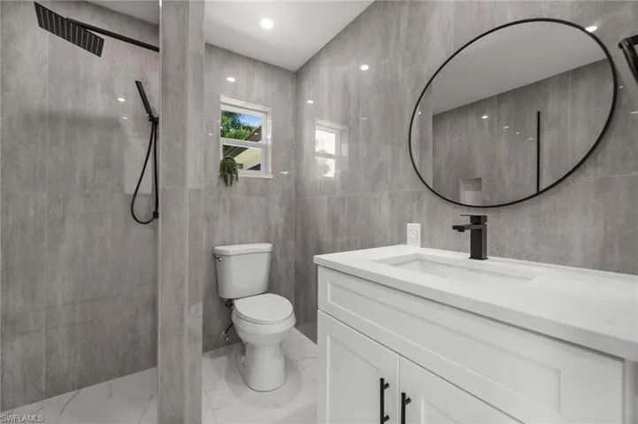 Full bath featuring vanity, tile walls, tiled shower, and marble finish flooring