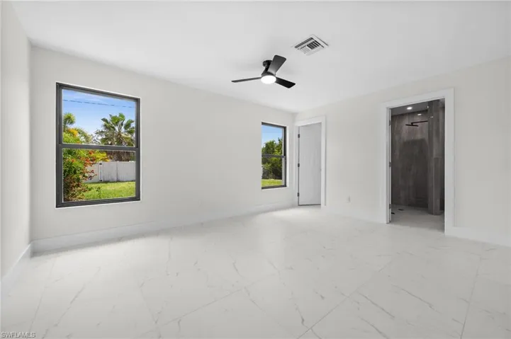Unfurnished bedroom featuring light marble finish flooring, a ceiling fan, and connected bathroom
