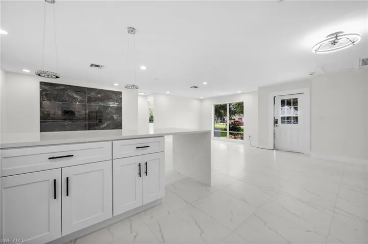 Kitchen featuring light marble finish floors, open floor plan, white cabinetry, hanging light fixtures, and light stone countertops