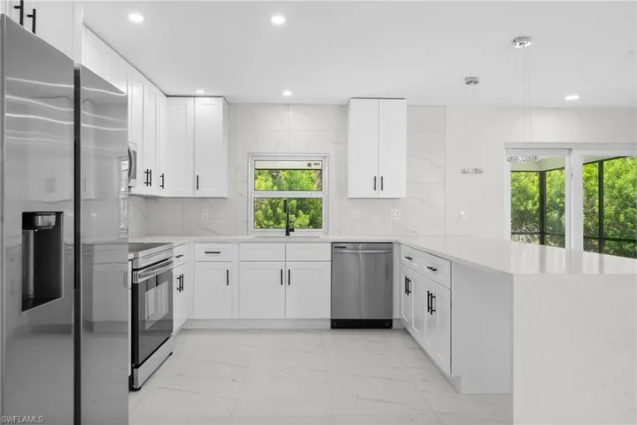 Kitchen with light marble finish floors, stainless steel appliances, a peninsula, pendant lighting, and white cabinetry