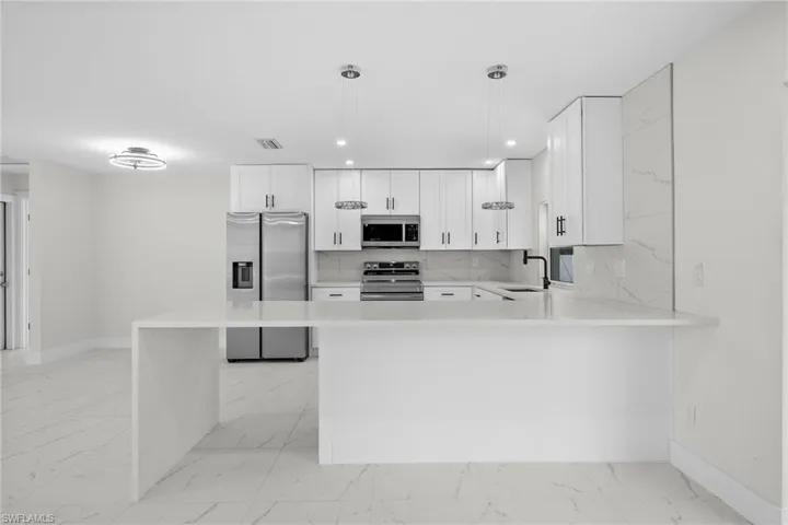 Kitchen featuring tasteful backsplash, stainless steel appliances, white cabinetry, light marble finish flooring, and recessed lighting