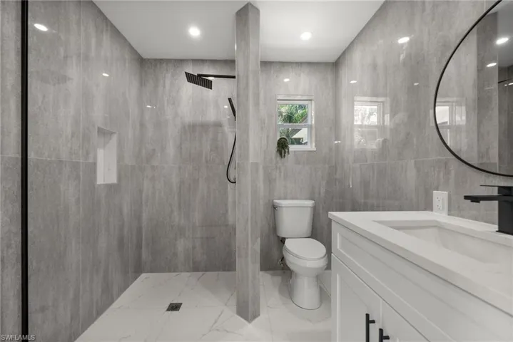 Bathroom featuring a walk in shower, vanity, tile walls, and light marble finish flooring