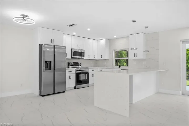 Kitchen with stainless steel appliances, backsplash, a peninsula, pendant lighting, and light stone countertops