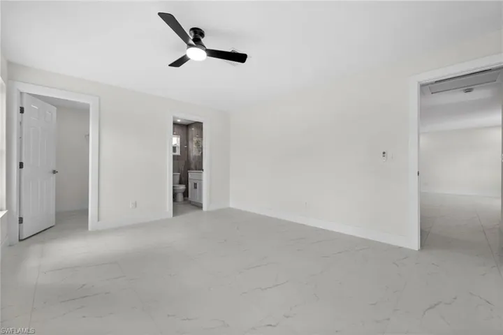 Unfurnished bedroom featuring a walk in closet, light marble finish flooring, a ceiling fan, and connected bathroom