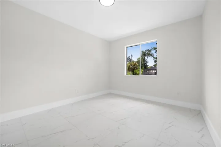 Unfurnished room featuring light marble finish flooring and baseboards