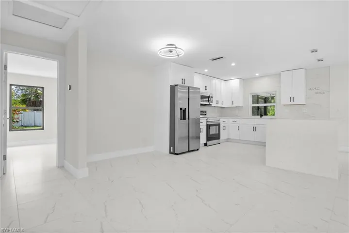 Kitchen with appliances with stainless steel finishes, light marble finish flooring, white cabinets, backsplash, and light stone countertops