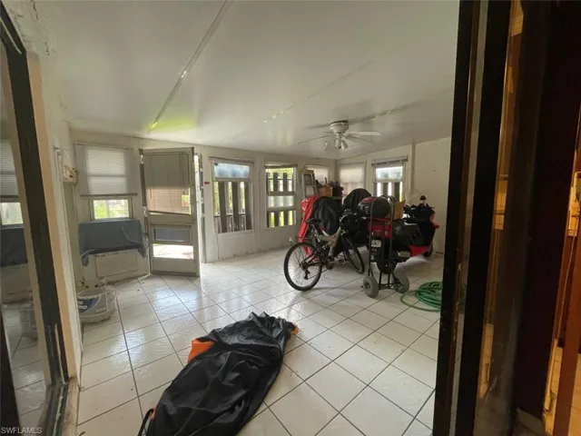Enclosed patio space featuring white square tile flooring, multiple windows providing ample natural light, and a ceiling fan with integrated lighting