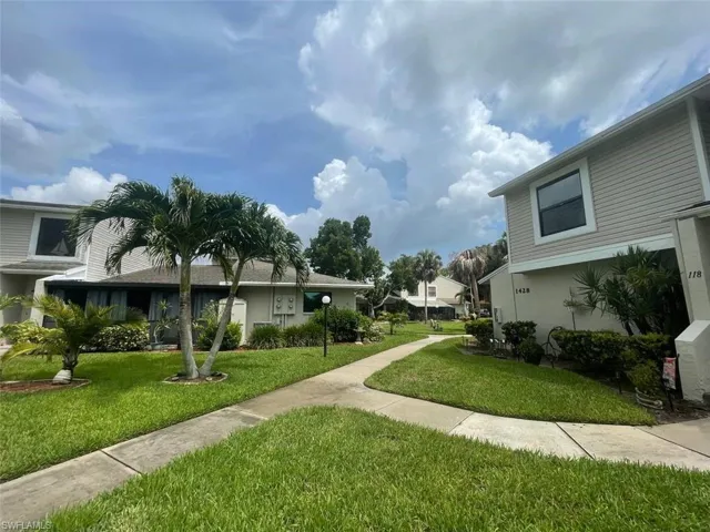 Exterior property featuring a concrete walkway, lush green lawn, mature palm trees, and established shrubbery