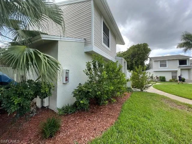 Exterior featuring light stucco and horizontal siding, with an established landscape bed, mature palm foliage, and a concrete pathway